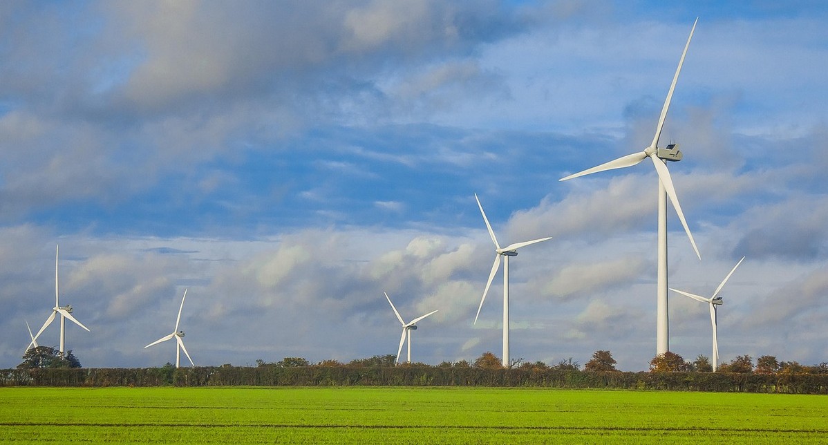 White wind turbines standing in a green field beneath a cloudy sky.