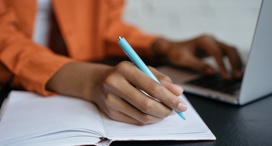 Person typing whilst holding a pen to a notebook